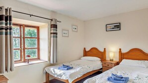 Una camera da letto con due letti singoli, una finestra con tende, un comodino con una lampada e un quadro appeso al muro.