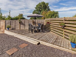 Eine Holzterrasse mit Tisch und Stühlen, umgeben von einem Holzzaun mit Blumentöpfen.