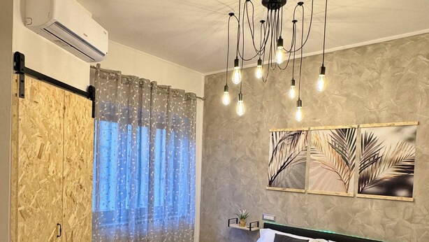 A bedroom with a bed, a wooden wardrobe, a curtain, a wall-mounted shelf, and a ceiling light fixture. - Del Regno Holiday House (Pompei)