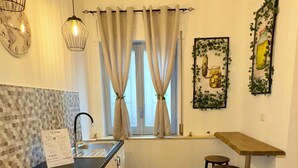 A kitchen with wooden cabinets, a black countertop, a sink, and a window with curtains. There are hanging lights and wall art. - Del Regno Holiday House (Pompei)