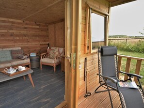 A wooden interior with a sofa, chairs, a table with teapot, and a window overlooking a grassy area. - 2 Bed in Okehampton (oc-63337) (Whiddon Down)