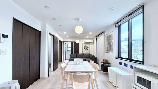 A modern kitchen with white appliances, a dining area with a table and chairs, and a large window with a city view.
