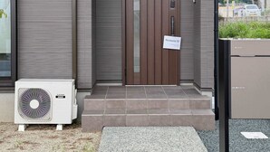 A modern building with a brown door, a sign reading 'Restavio Ozu 053,' and a large air conditioning unit outside.