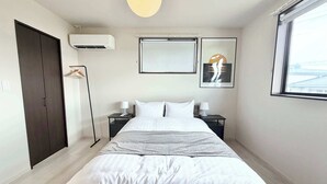 A bedroom with a bed, bedside tables, an air conditioning unit, a wardrobe, and a window.