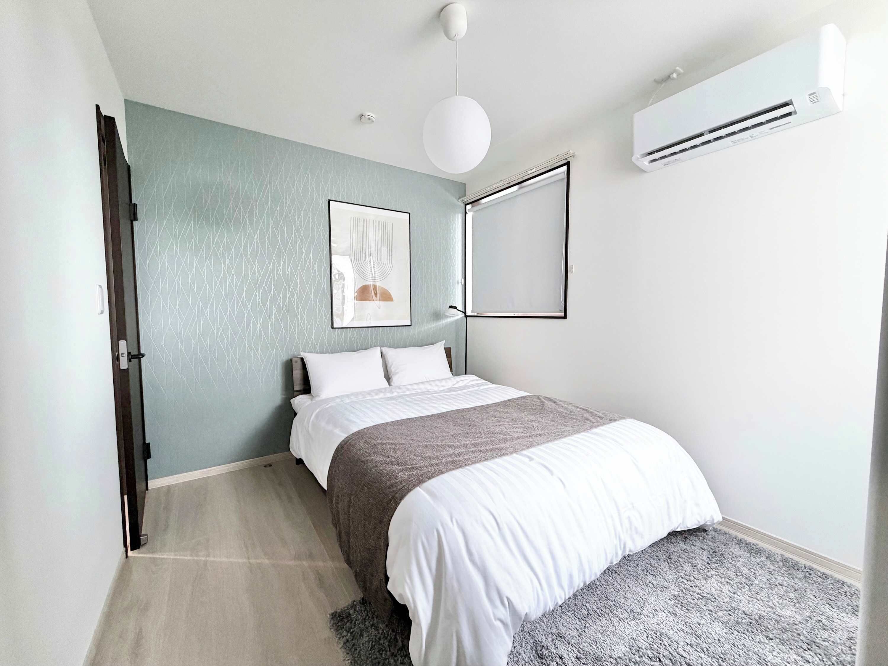 A modern bedroom with a bed, a wall-mounted air conditioner, and a ceiling light fixture.