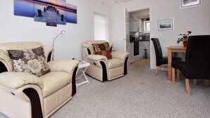 Ein modernes Wohnzimmer mit zwei beigefarbenen Sofas, einem kleinen Tisch und einem Essbereich mit Holztisch und Stühlen.