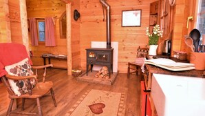 A cozy cabin interior with a wood-burning stove, a rocking chair, a dining table, and a kitchen area.