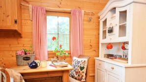 A wooden cabin interior with a wooden table, a chair, a cabinet, and a window with curtains.