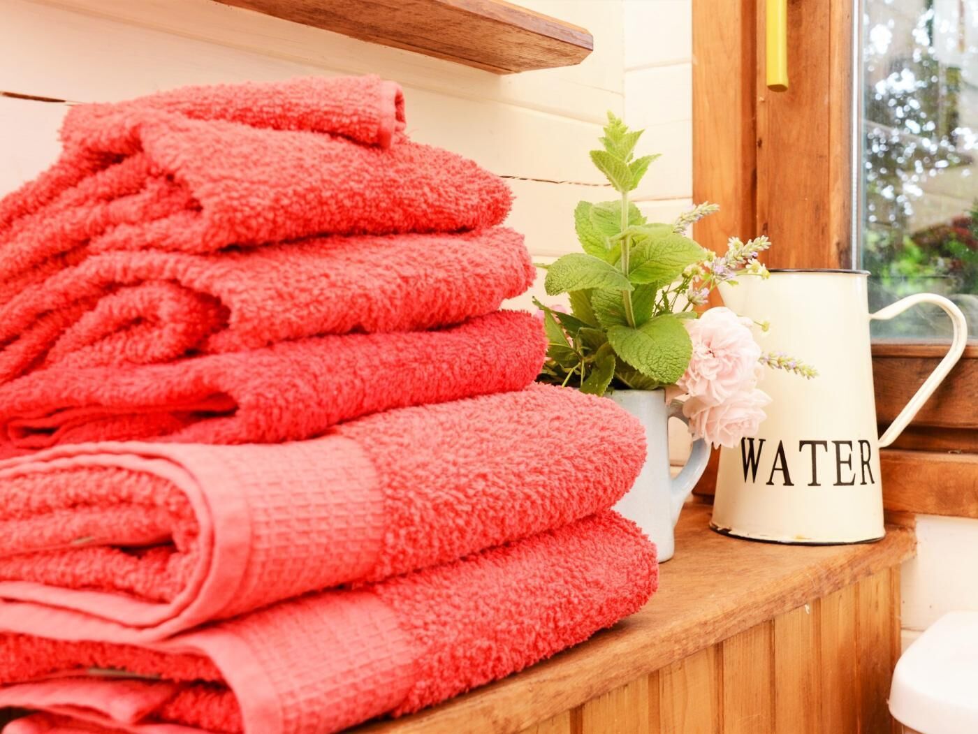 A stack of red towels, a white mug with 'WATER' written on it, and a window with a view of greenery.