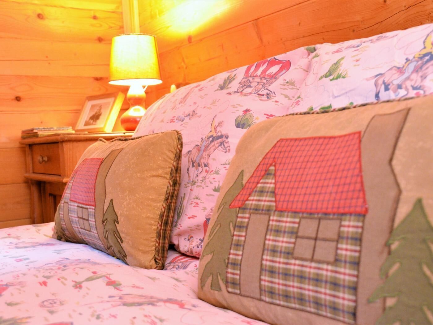 A wooden cabin interior with a bed featuring floral and plaid-patterned pillows.