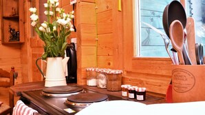 A kitchen with wooden walls, a stove, a kettle, jars of condiments, and a window with utensils.