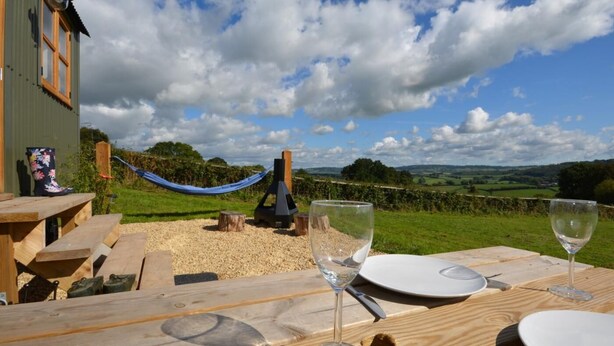 A wooden table with a wine glass and plates, a hammock, and a view of the countryside. - 1 Bed in Usk- (oc-63292) (Llangwm)