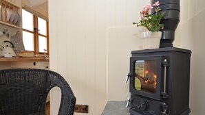 Ein Zimmer mit einem schwarzen Kaminofen, einem Korbstuhl und einem Steinkamin.