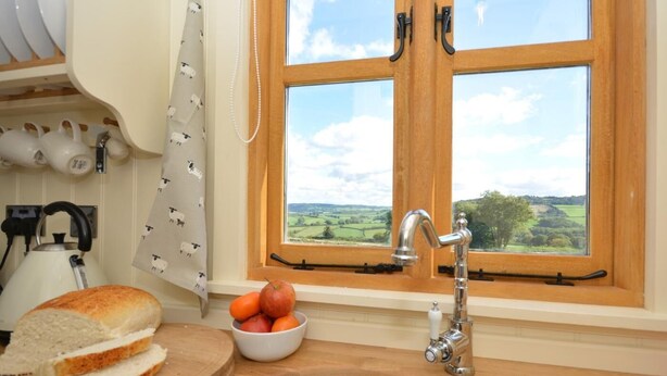 Eine Küche mit Spülbecken aus Edelstahl, einem Wasserkocher, einer Obstschale und einem Fenster mit Blick ins Grüne.