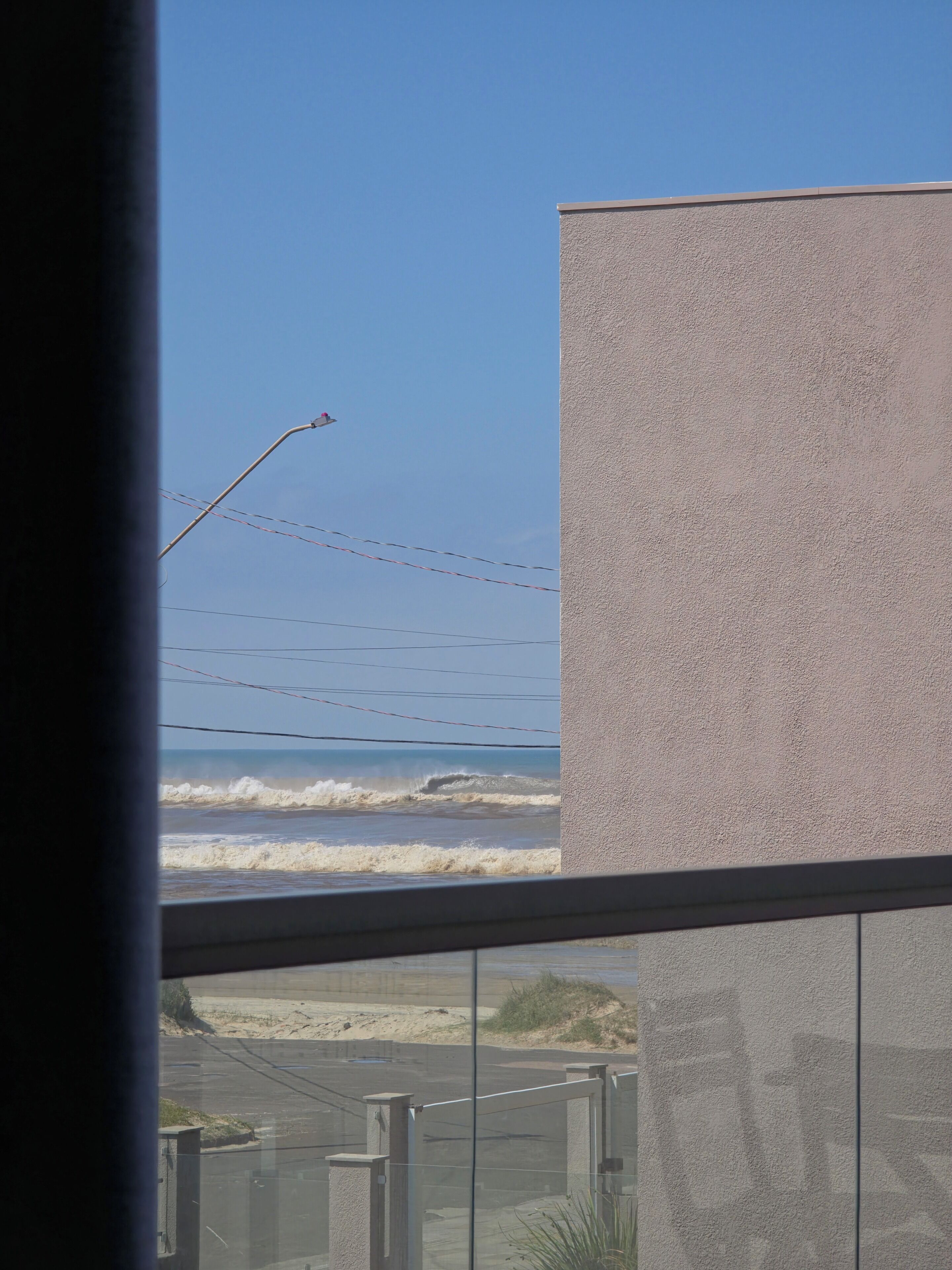 Blick auf das Meer mit brechenden Wellen, eine Straßenlaterne und ein Gebäude mit strukturierter Fassade.