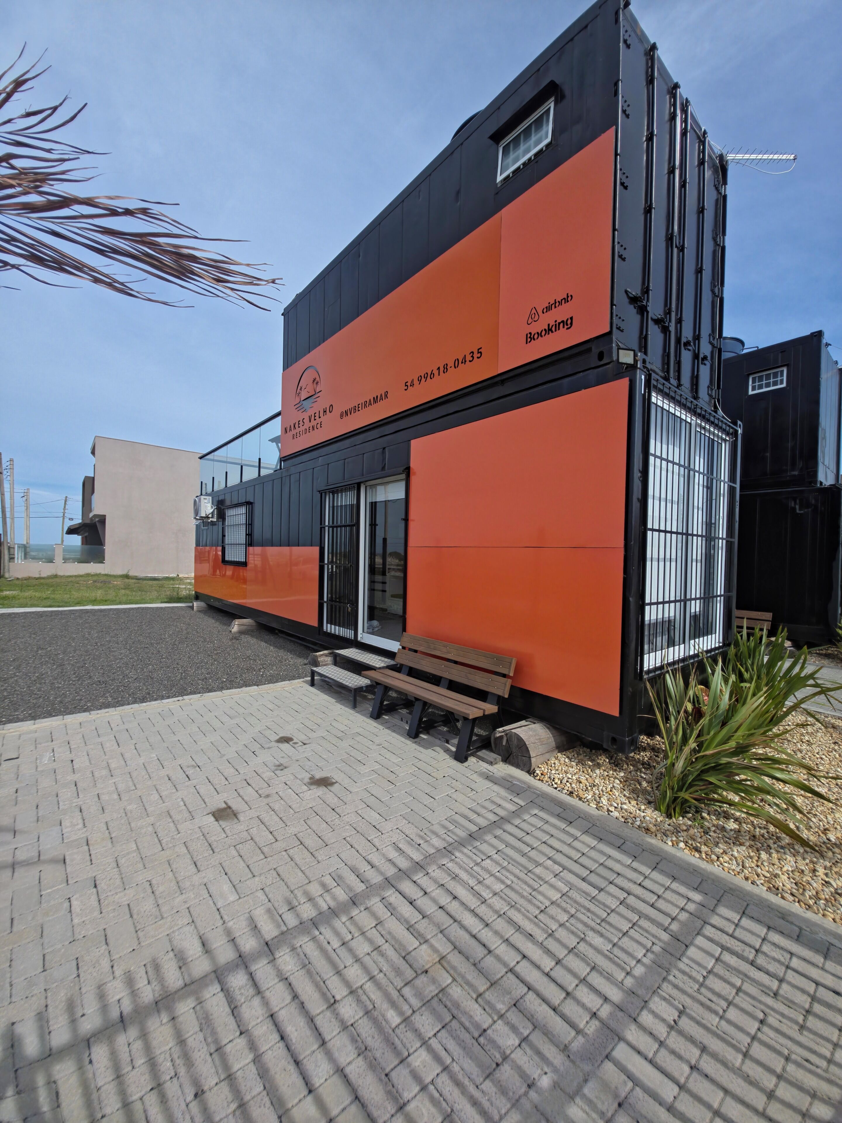 A modern building with a black and orange facade, a bench outside, and a clear sky.