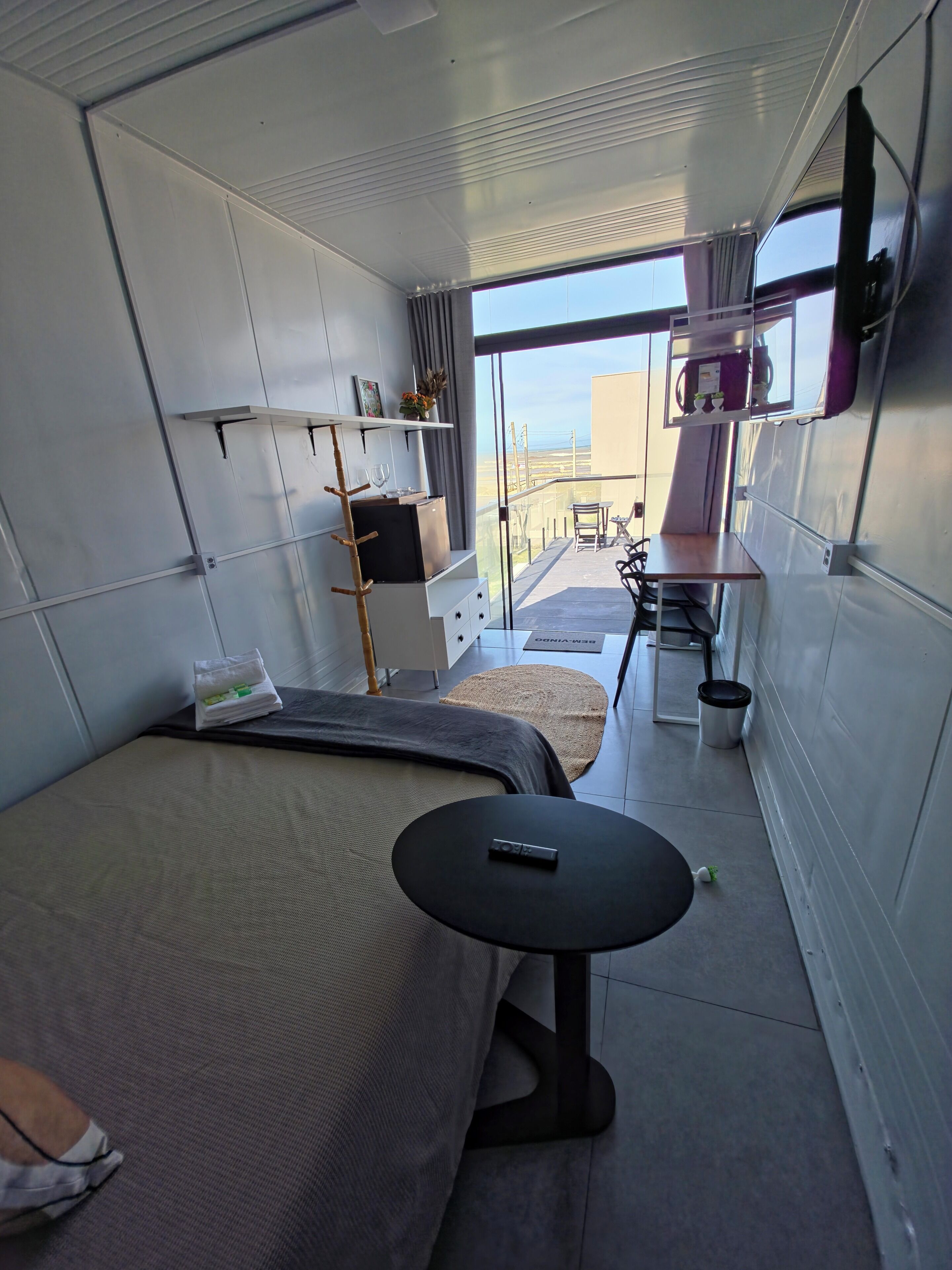 A compact room with a bed, a small table, a sofa, a TV, and a balcony with a view.