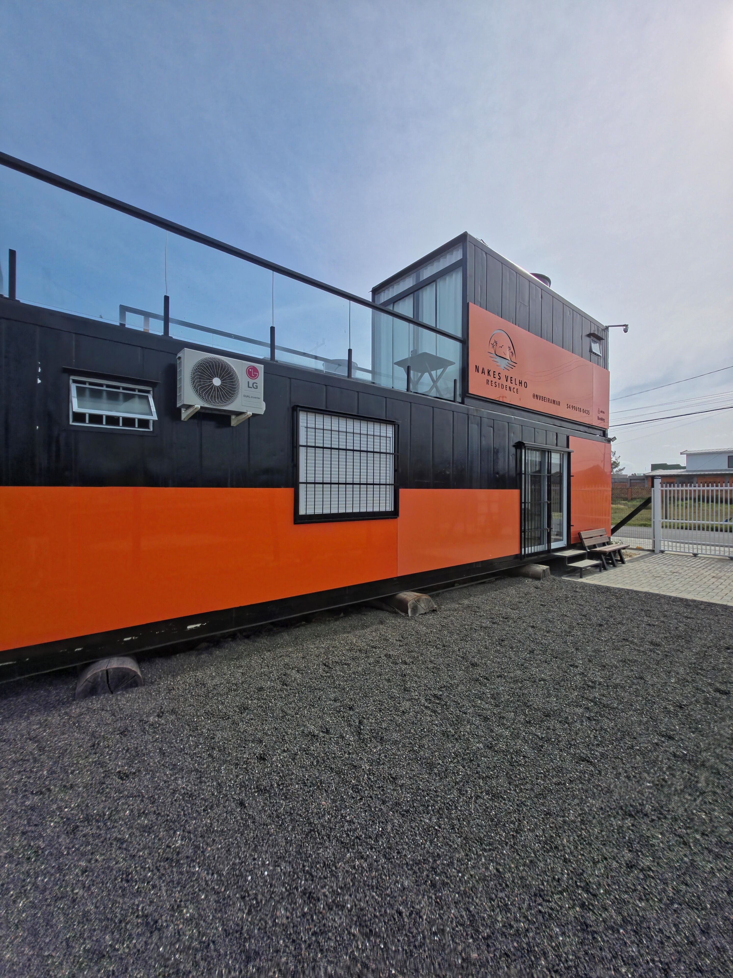 A modern building with a black and orange facade, a large air conditioning unit, and a clear sky.