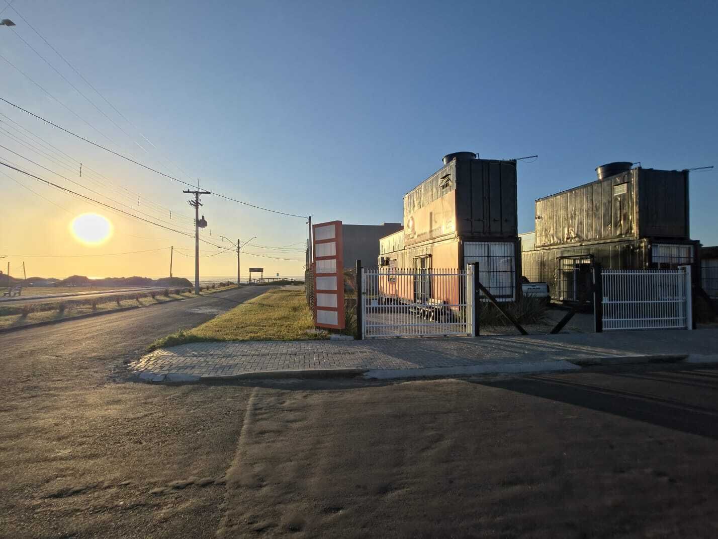 A large industrial building with a gated entrance, surrounded by a paved area and a road.