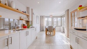 Una cocina moderna con armarios blancos, un comedor con mesa y sillas, y vistas amplias a través de grandes ventanales.