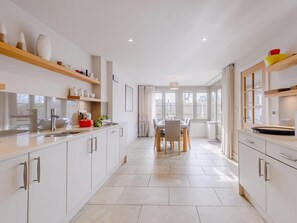 Eine moderne Küche mit weißen Schränken, ein Essbereich mit Tisch und Stühlen sowie ein Ausblick durch große Fenster.