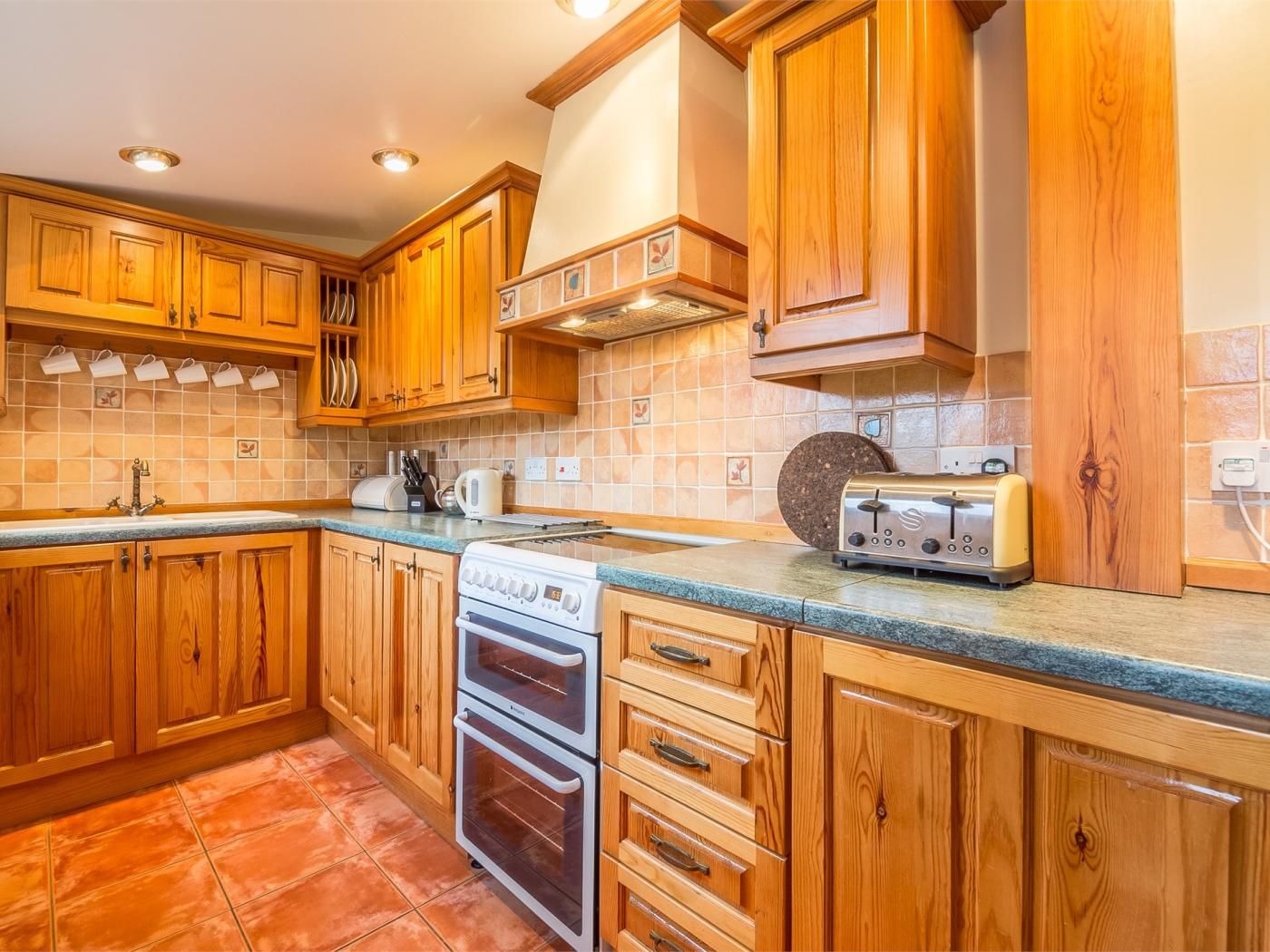 Eine Küche mit Holzausstattung, einem eingebauten Backofen, einem Toaster und einer gefliesten Spritzschutzwand.