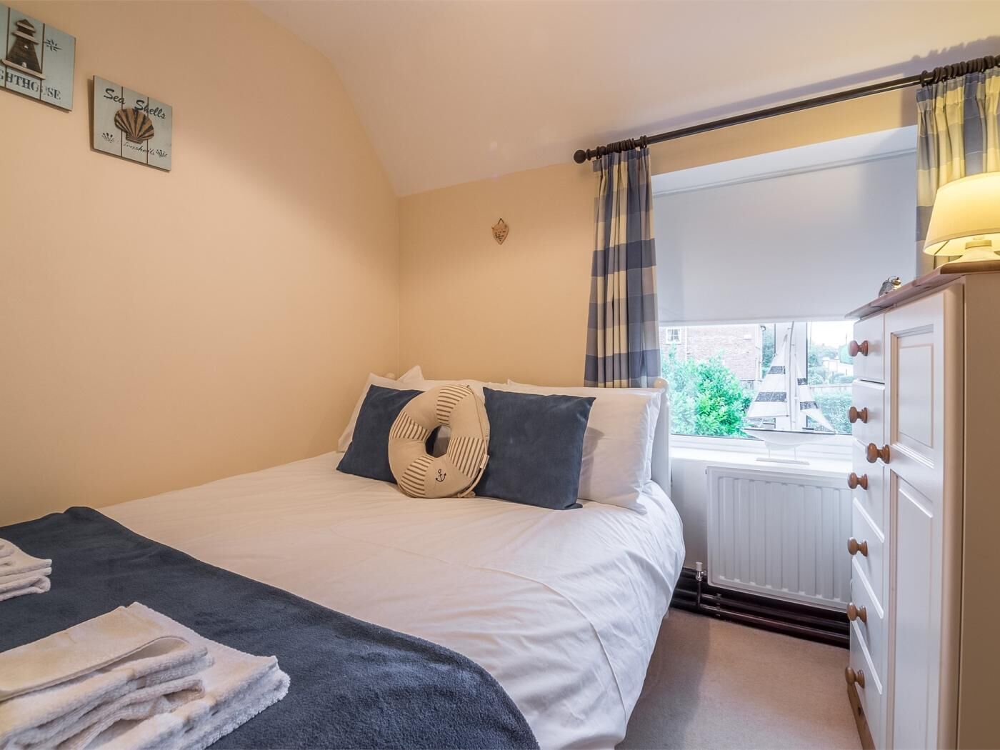 Un dormitorio con cama, ventana con cortinas, cómoda y adornos en la pared.