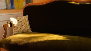 A green upholstered sofa with a patterned pillow, positioned in a room with a wooden chair and a painting on the wall.