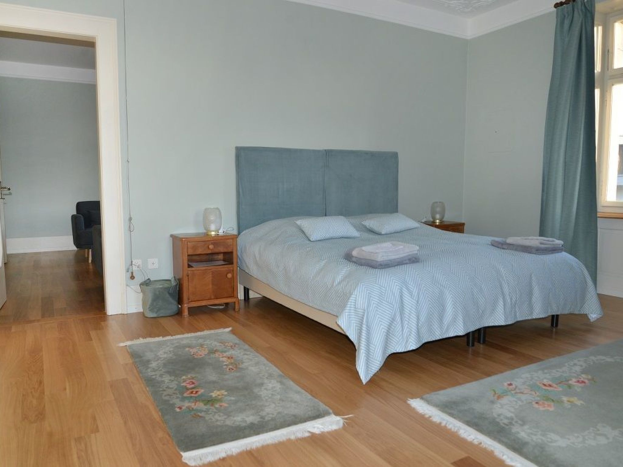 A bedroom with a bed, two bedside tables, a nightstand, a chair, and a window with curtains.