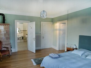 Een slaapkamer met een bed, een stoel, een radiator en een deur naar een badkamer.