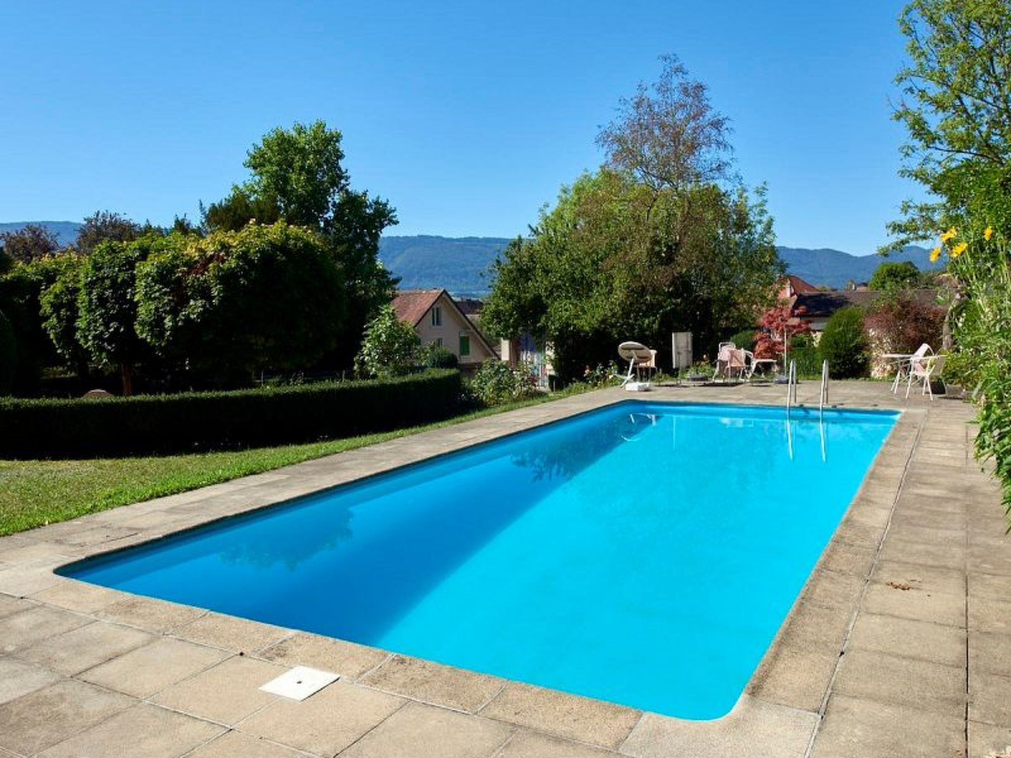 Una piscina rectangular con superficie de agua azul cristalina, rodeada por un solárium empedrado.