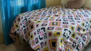 Une chambre avec une couvre-lit à motifs, une tête de lit blanche, un oreiller moelleux et des rideaux bleus.