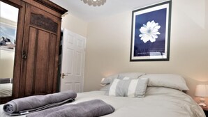 Ein ordentlich bezogenes Bett mit Kissen, ein Holzschrank und ein gerahmtes Bild an der Wand.