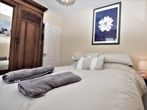 Ein ordentlich bezogenes Bett mit Kissen, ein Holzschrank und ein gerahmtes Bild an der Wand.