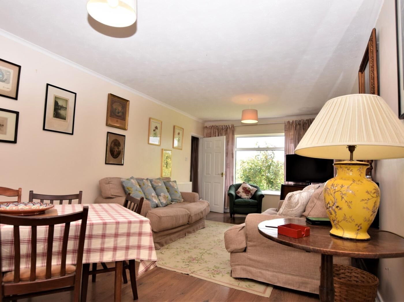 Een woonkamer met een eettafel, banken, een televisie en een gele lamp.