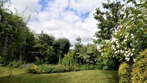 Ein gepflegter Garten mit verschiedenen Pflanzen und Blumen, bewölkter Himmel und einem Rasen.