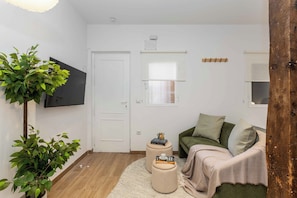 A living room with a sofa, ottomans, a plant, and a flat-screen TV mounted on the wall. - A studio in the heart of Malasaña's creative quarter, where every corner has been composed like a gallery you get to live in. (MADRID)