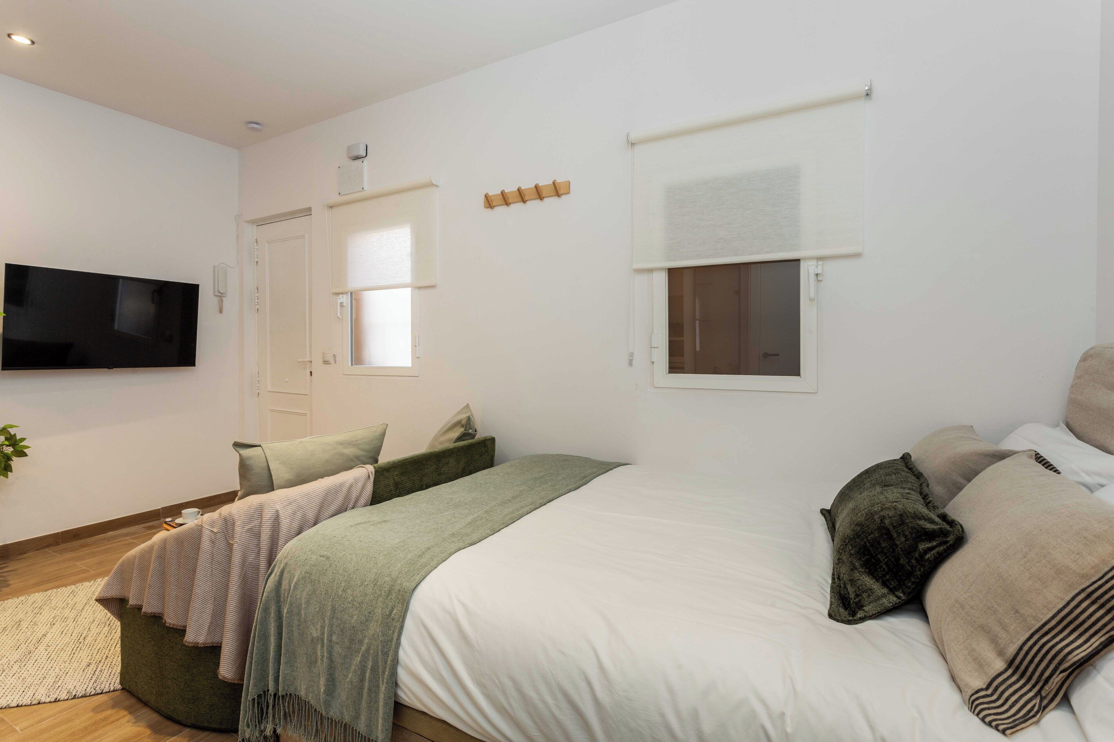 A bedroom with a bed, a TV, a window, and a door.