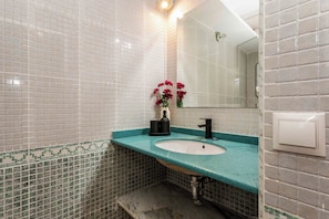 A bathroom with a white sink, teal countertop, and a mirror. - A studio in the heart of Malasaña's creative quarter, where every corner has been composed like a gallery you get to live in. (MADRID)