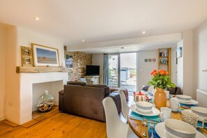 Ein Wohnzimmer mit einer Couch, einem Esstisch gedeckt mit Tellern, Tassen und einer Blumenvase.