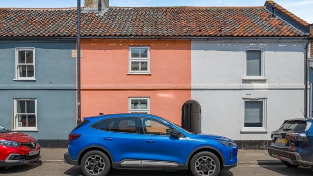 Ein blaues Auto vor einem Gebäude mit roter und weißer Fassade, ein rotes Auto links und ein blaues Auto rechts.