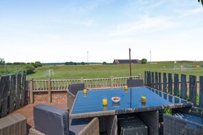 An outdoor patio with a table and chairs, a view of a sports field, and a brick wall. - 3 Bed in Wells-next-the-sea (oc-kt050) (Wells-next-the-Sea)