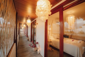 Een gang met houten vloer, een bed met wit beddengoed en een hanglamp.