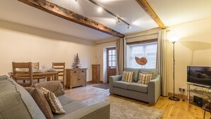 Ein Wohnzimmer mit einer Couch, einem Esstisch mit Stühlen, einem Fernseher und einer Zimmerpflanze.