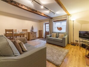 Ein Wohnzimmer mit einer Couch, einem Esstisch mit Stühlen, einem Fernseher und einer Zimmerpflanze.