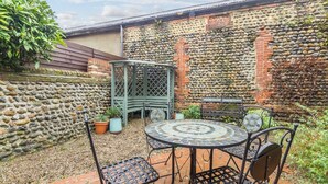 Eine Terrasse mit rundem Tisch und Stühlen, einer grünen Rankgitterstruktur und einer Steinmauer.