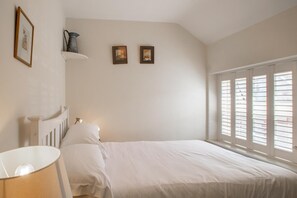 Ein Schlafzimmer mit einem Bett, einem Nachttisch, einer Lampe, einem Regal mit Dekoration und einem Fenster mit Jalousien.