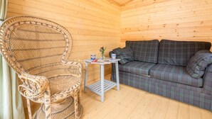 Un interior de madera con una silla de mimbre, un sof á de cuadros y una mesita con una taza y un florero.