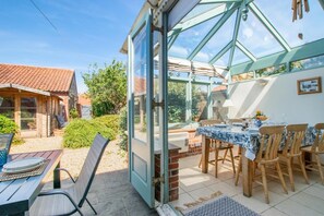 Une véranda avec un coin repas, une table dressée pour quatre personnes et une vue sur le jardin.