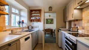 Una cocina con lavavajillas, horno y comedor con mesa y sillas.